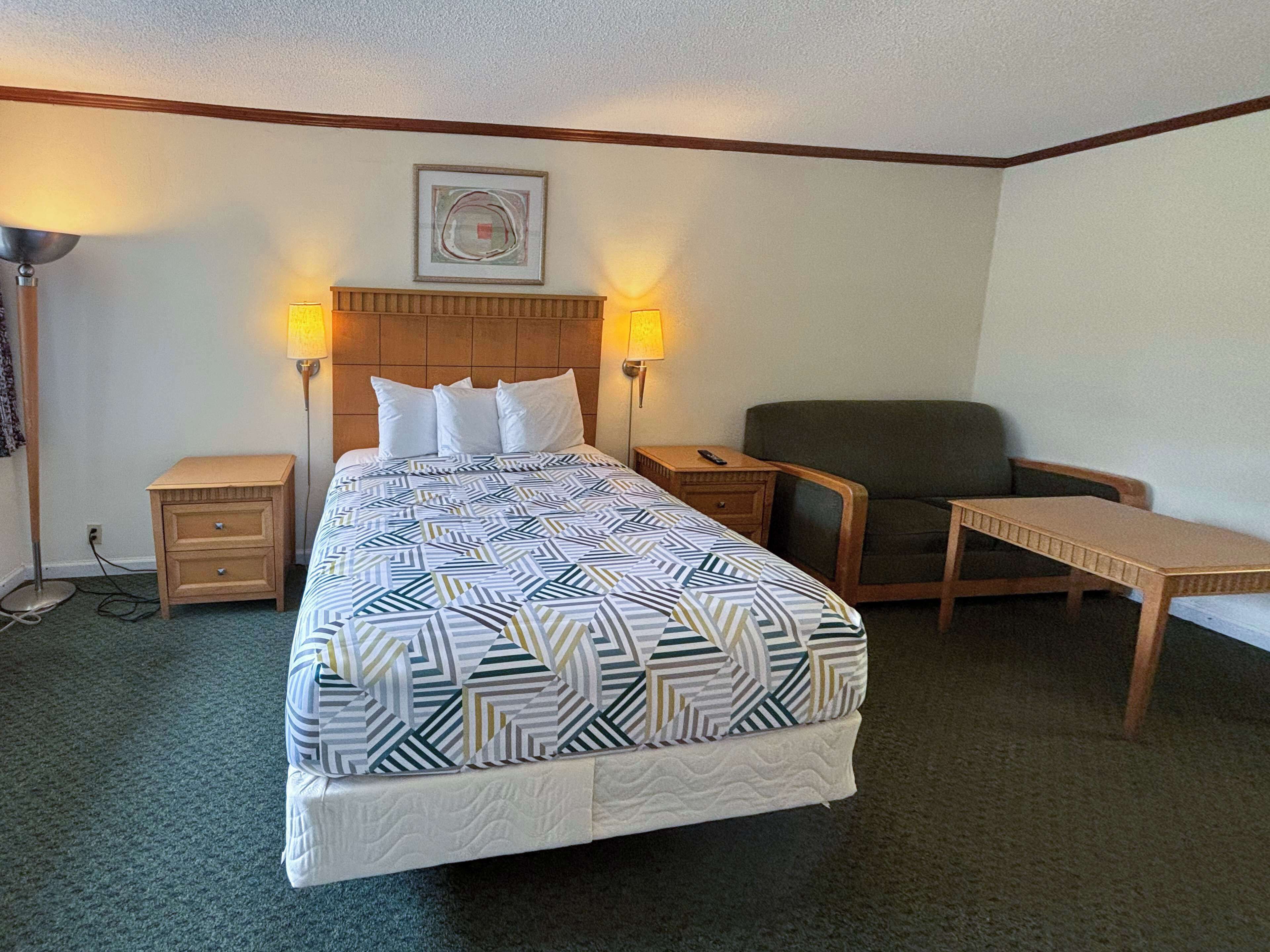 Una habitación de hotel con una cama, dos mesitas de noche, una silla y una pequeña mesa.