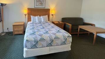 Una habitación de hotel con una cama, dos mesitas de noche, una silla y una pequeña mesa.