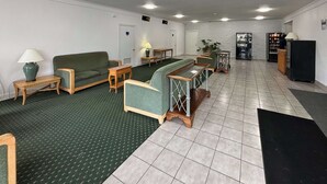 Una hall d'albergo con tappeto verde, arredi in legno, una reception, distributori automatici e un frigorifero.