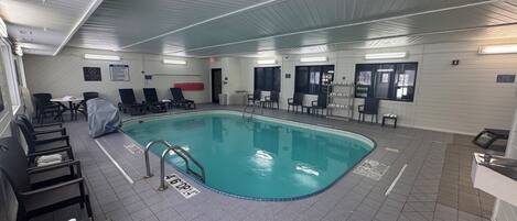 An indoor swimming pool with a tiled floor, lounge chairs, and a covered seating area.