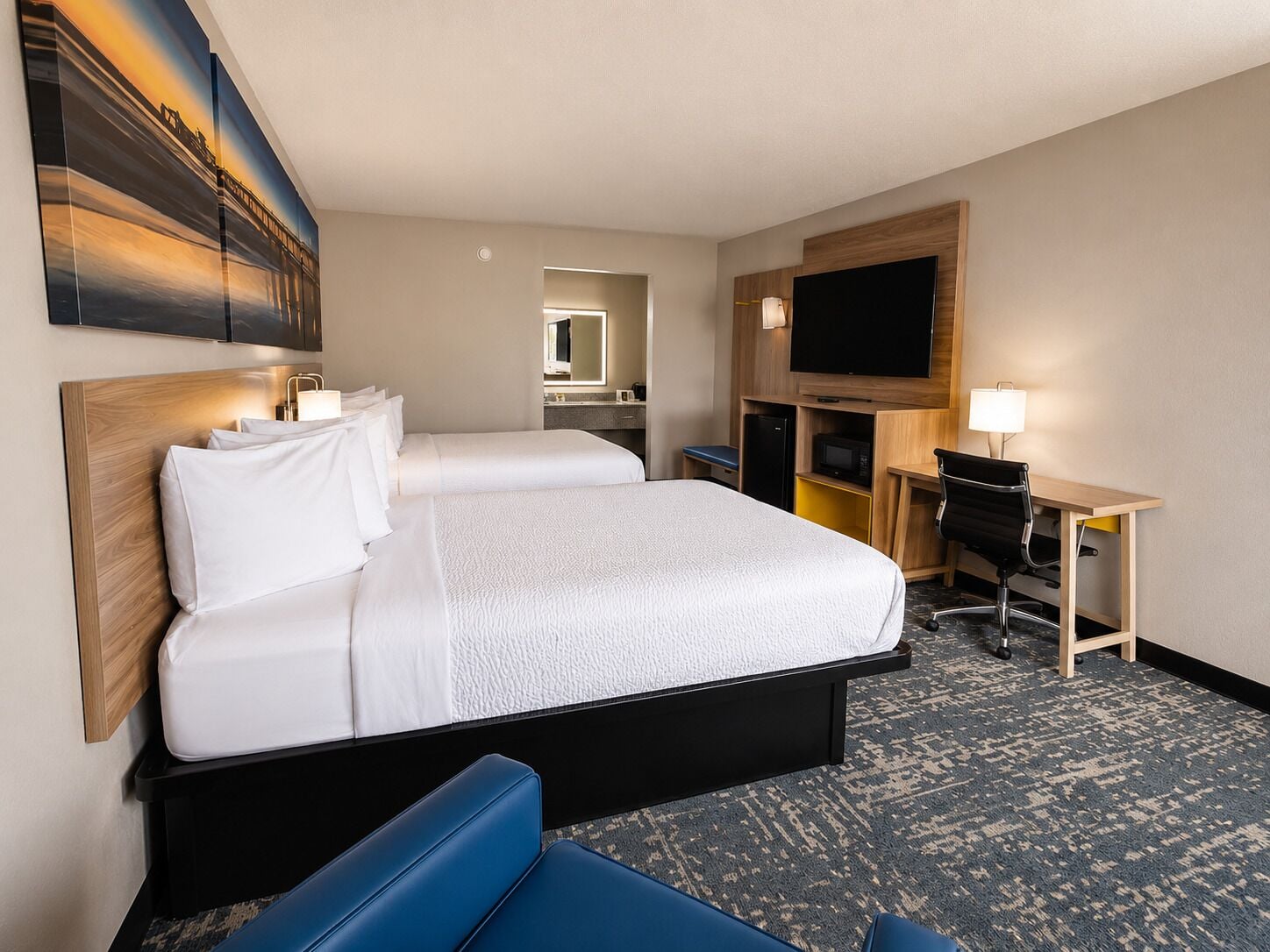 Quarto de hotel com uma cama grande, uma mesa com cadeira, televisão de tela plana e um quadro na parede.