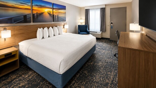 Habitación de hotel con una cama grande, un escritorio, una silla, un televisor y tres cuadros en la pared.