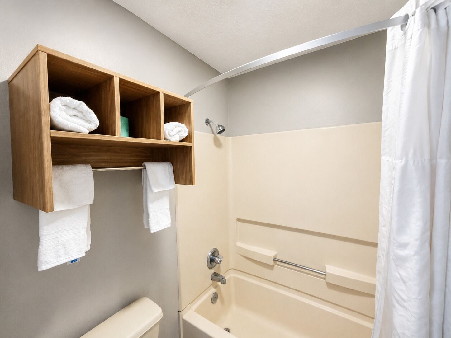 A bathroom with a wooden shelf holding towels, a toilet, and a bathtub with a shower curtain.