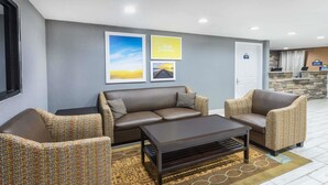 Un vestíbulo moderno con pared gris, sofá marrón, sillones estampados, una mesa de centro oscura y un mostrador de recepción con fondo de piedra.