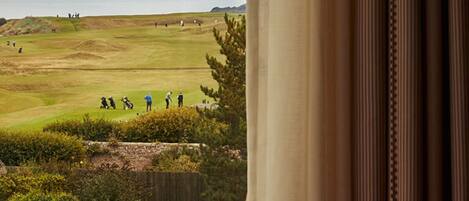 Vista desde una ventana sobre un campo de golf con una isla en la distancia.