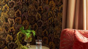A room with patterned wallpaper, a wicker table with a glass and plant, and a red upholstered chair.
