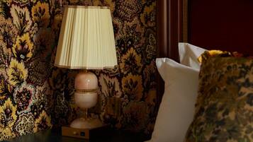 A bedroom with a bed, a nightstand with a lamp, and floral wallpaper.