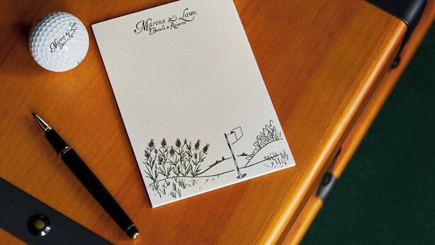 A wooden table with a white card, a golf ball, and a pen. - Marine North Berwick (North Berwick)