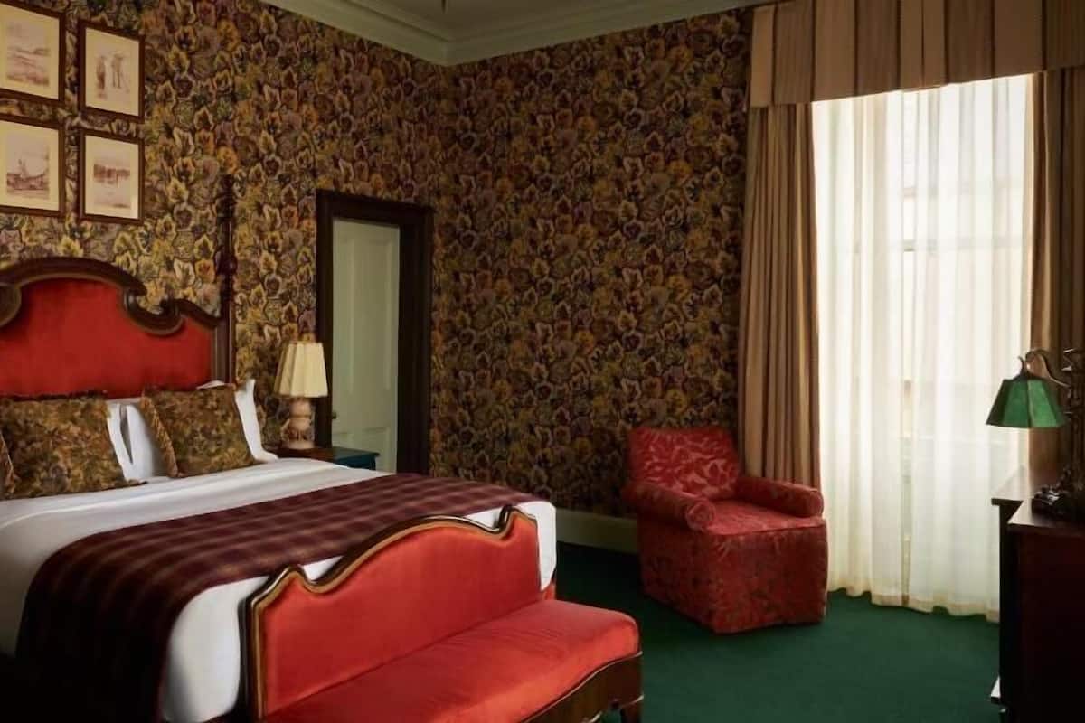 Quarto com cama grande, poltrona vermelha, mesa de cabeceira e cômoda.