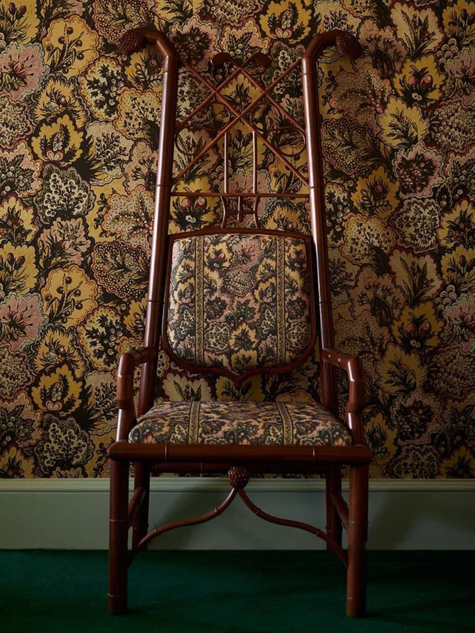A chair with a high backrest and a cushioned seat, positioned against a wall with a floral patterned wallpaper.