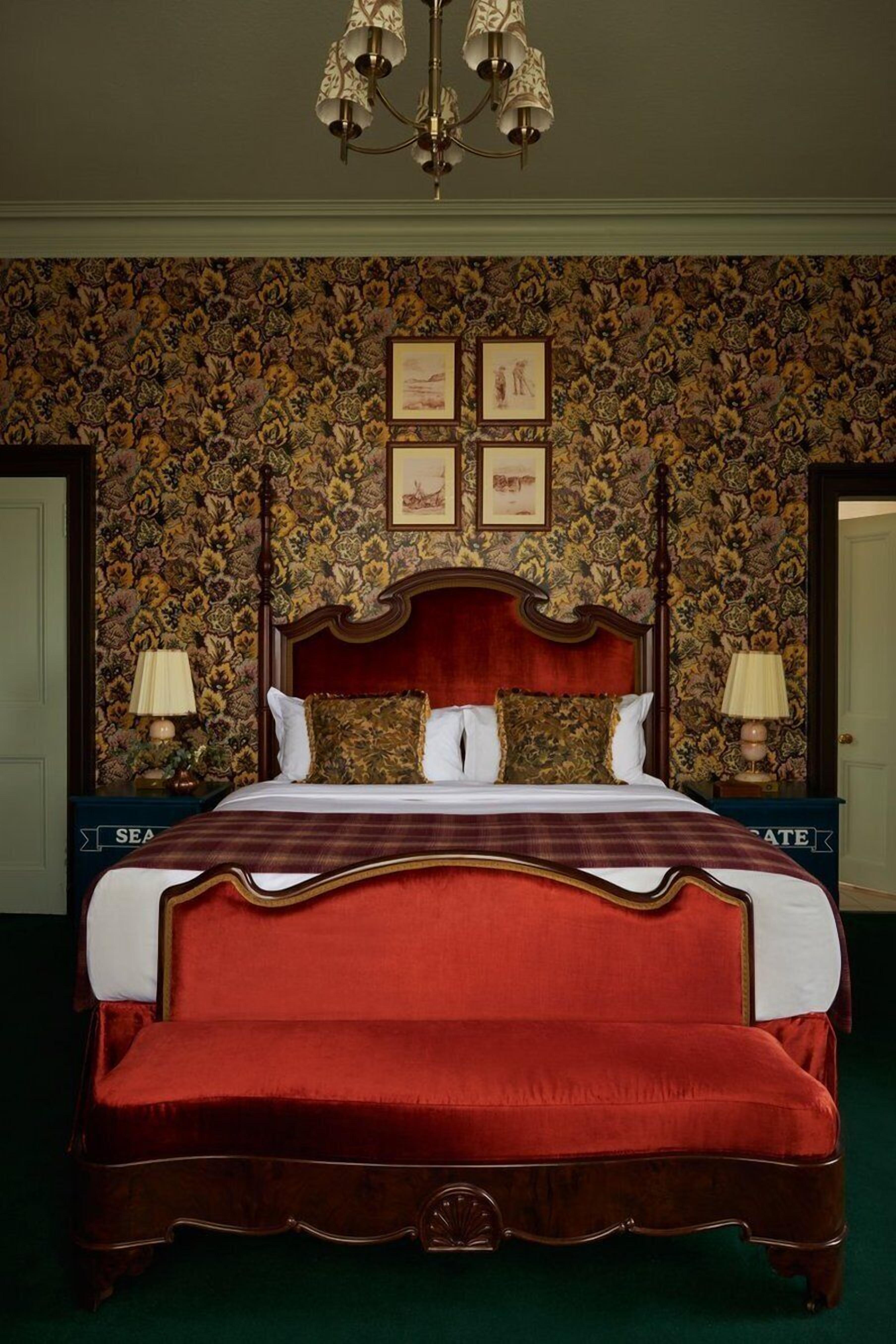 Un grand lit avec une tête de lit rouge, deux tables de chevet avec des lampes et un papier peint à motifs floraux.