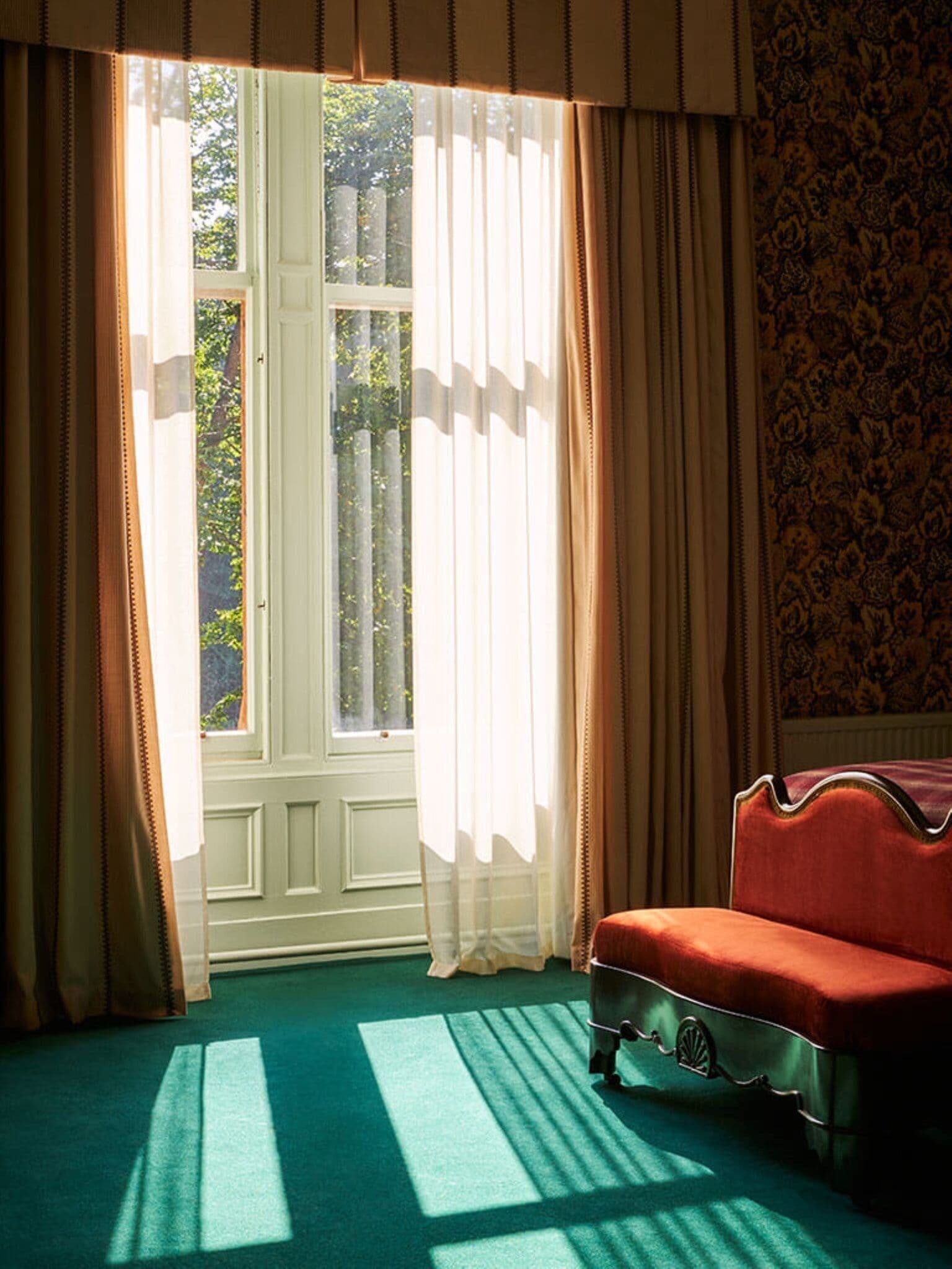 A room with a large window, a red sofa, and a patterned wallpaper.