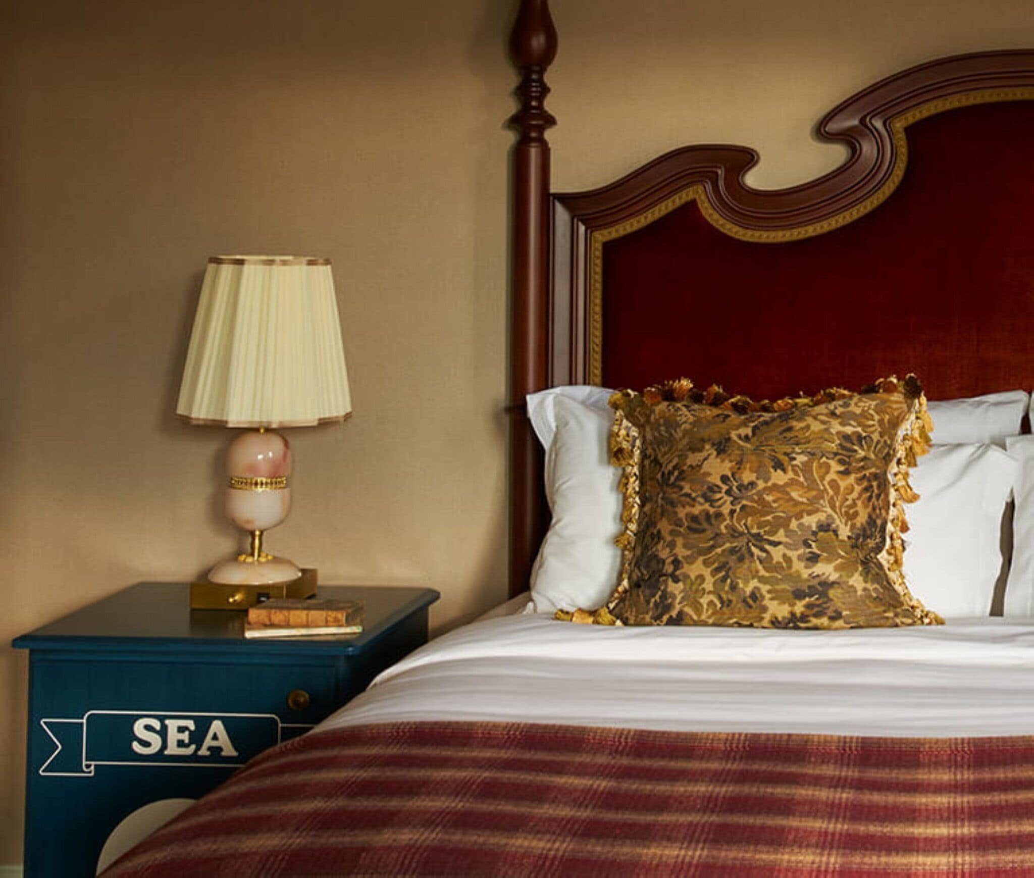 A neatly made bed with a red headboard, a decorative pillow, and a lamp on a nightstand with a 'SEA' sign.