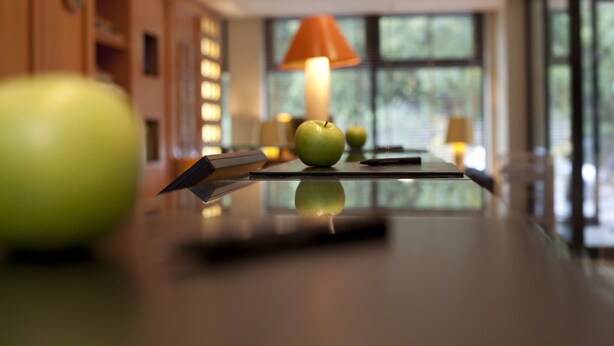 A modern kitchen with a reflective countertop, green apples, and a table lamp.