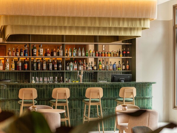 Eine Bar mit mehreren Spirituosenflaschen, einem Computermonitor und Barhocker.
