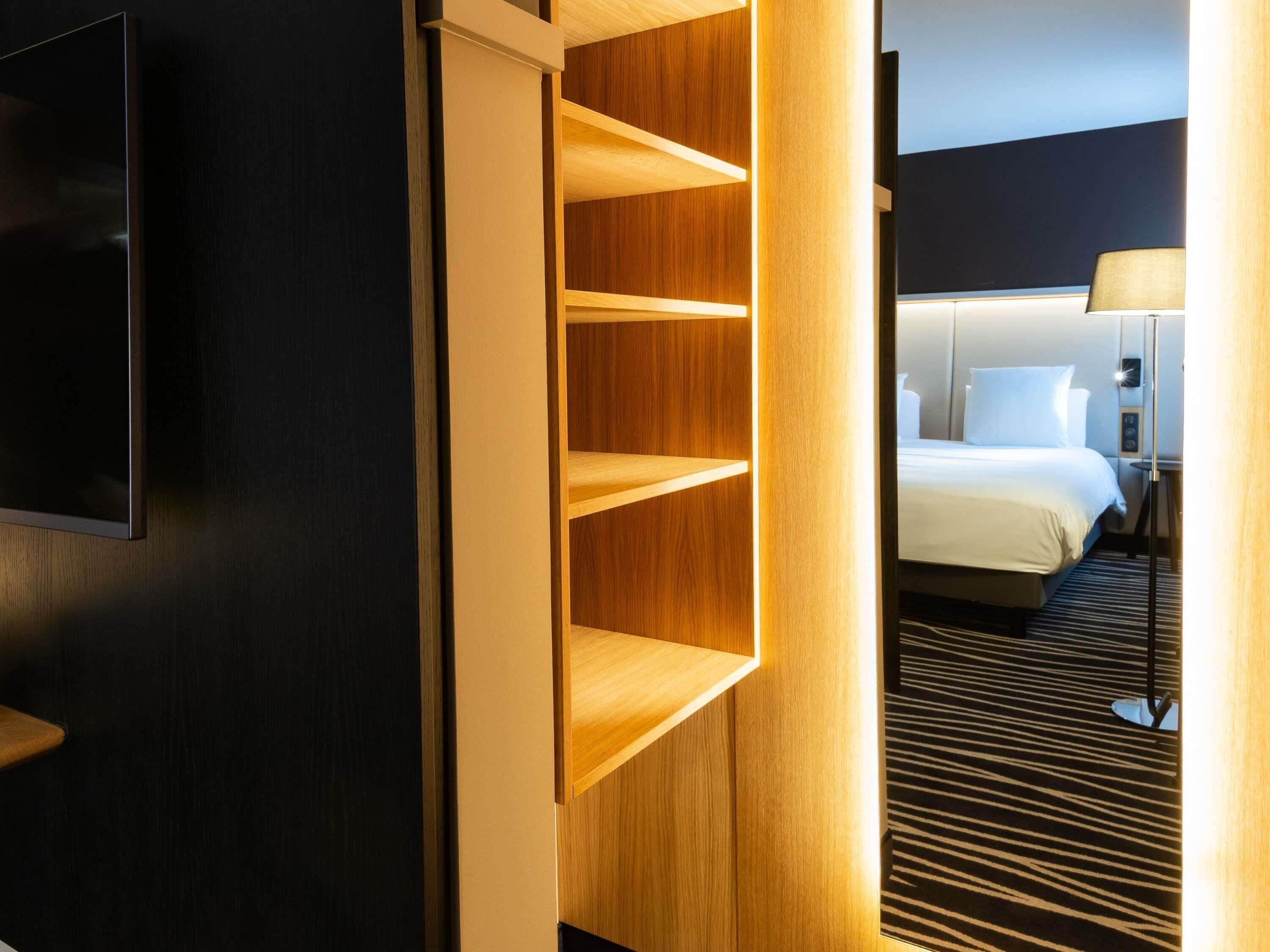 Una habitación de hotel con una cama, un televisor montado en la pared y un estante de madera.
