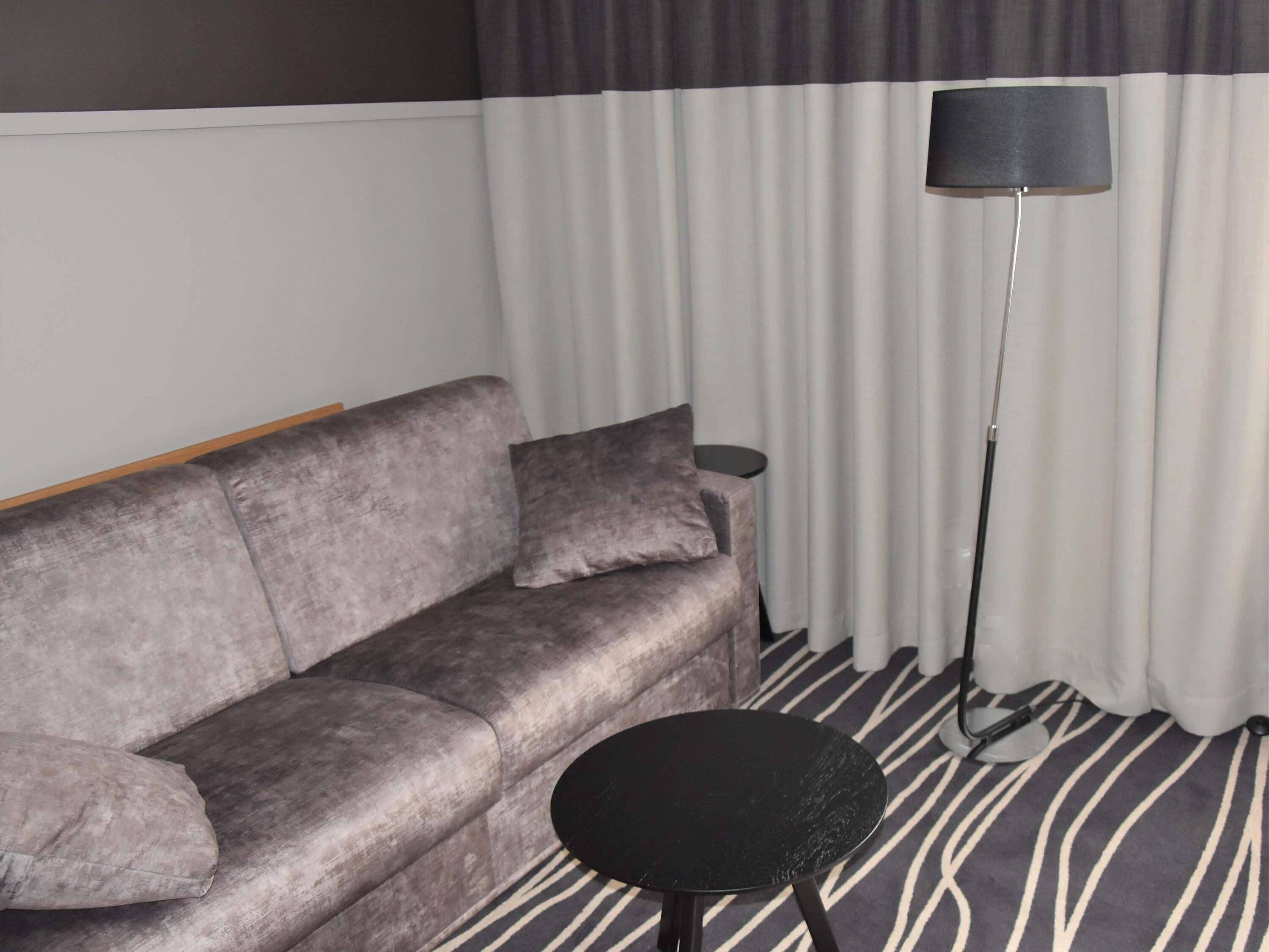 Un sofá gris con una mesita auxiliar negra y una lámpara de pie en una habitación con alfombra a rayas.