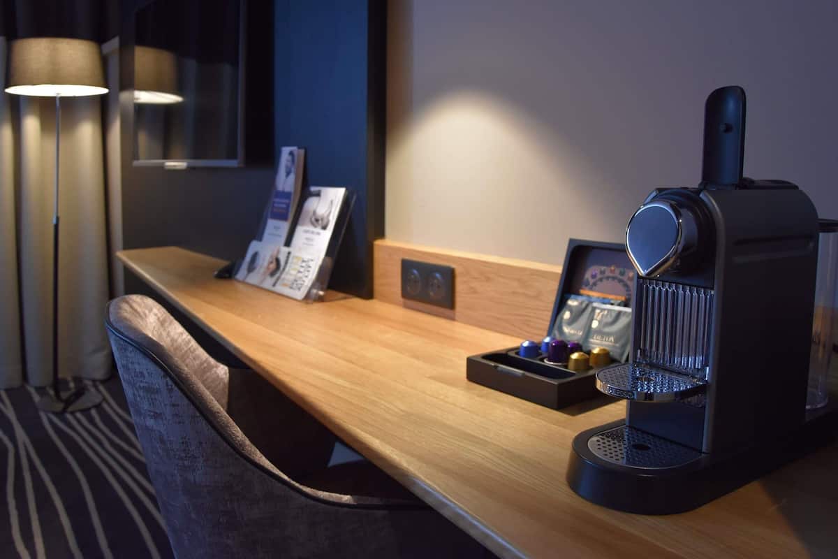 A hotel room with a wooden desk, a coffee machine, a framed picture, and a small tray with items.