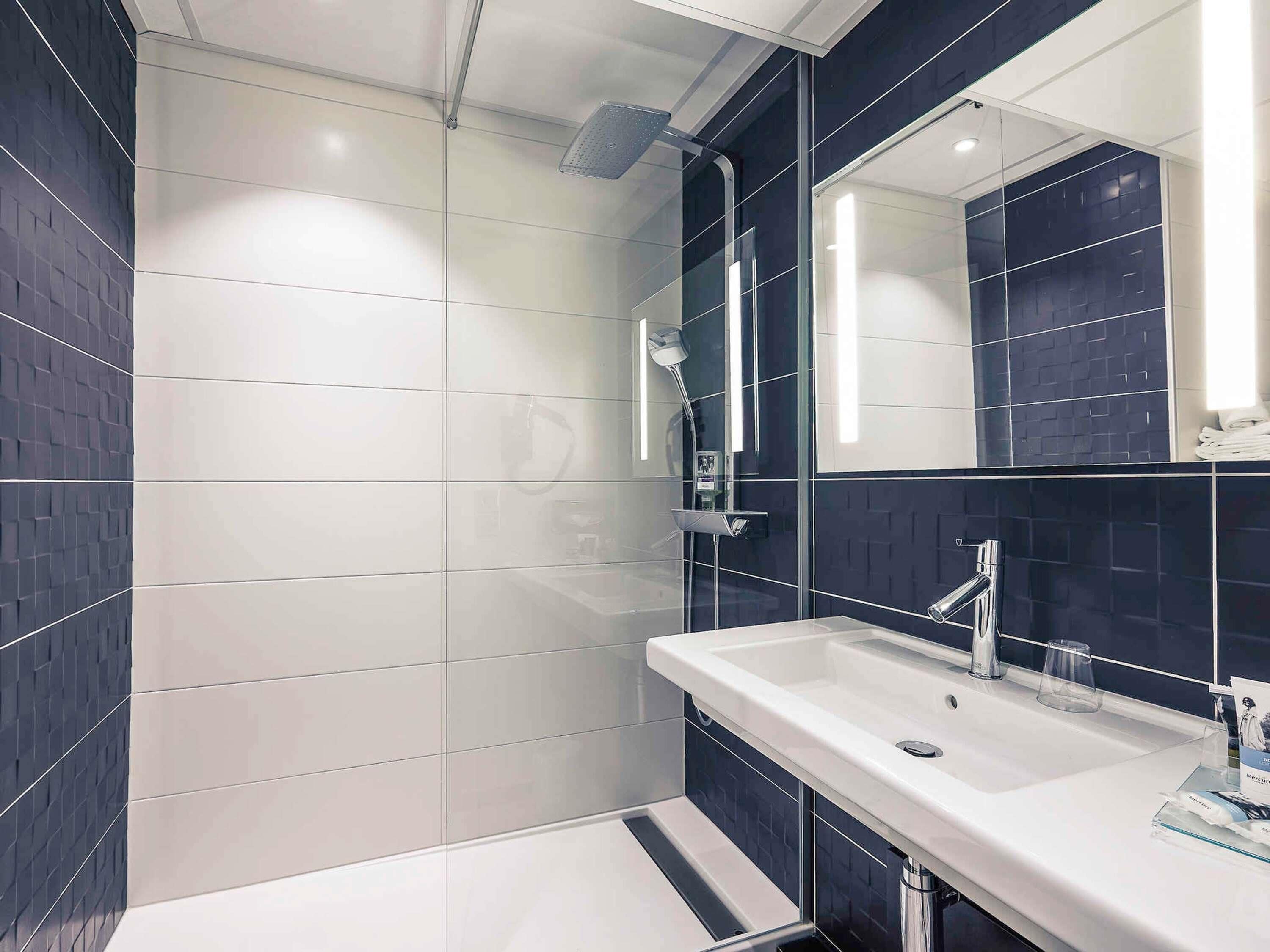 Un baño moderno con lavamanos blanco, un espejo grande y una ducha.