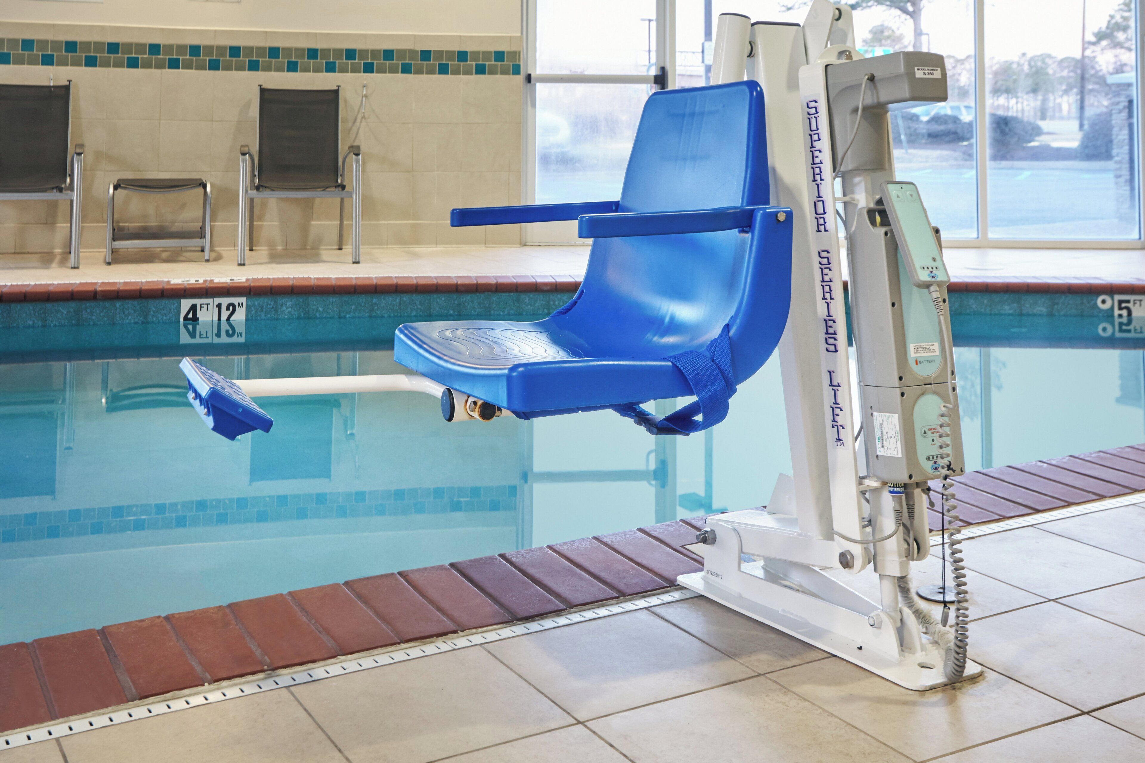 A poolside chair attached to a lift system, a pool with a tiled edge, and a window with a view of the outside.