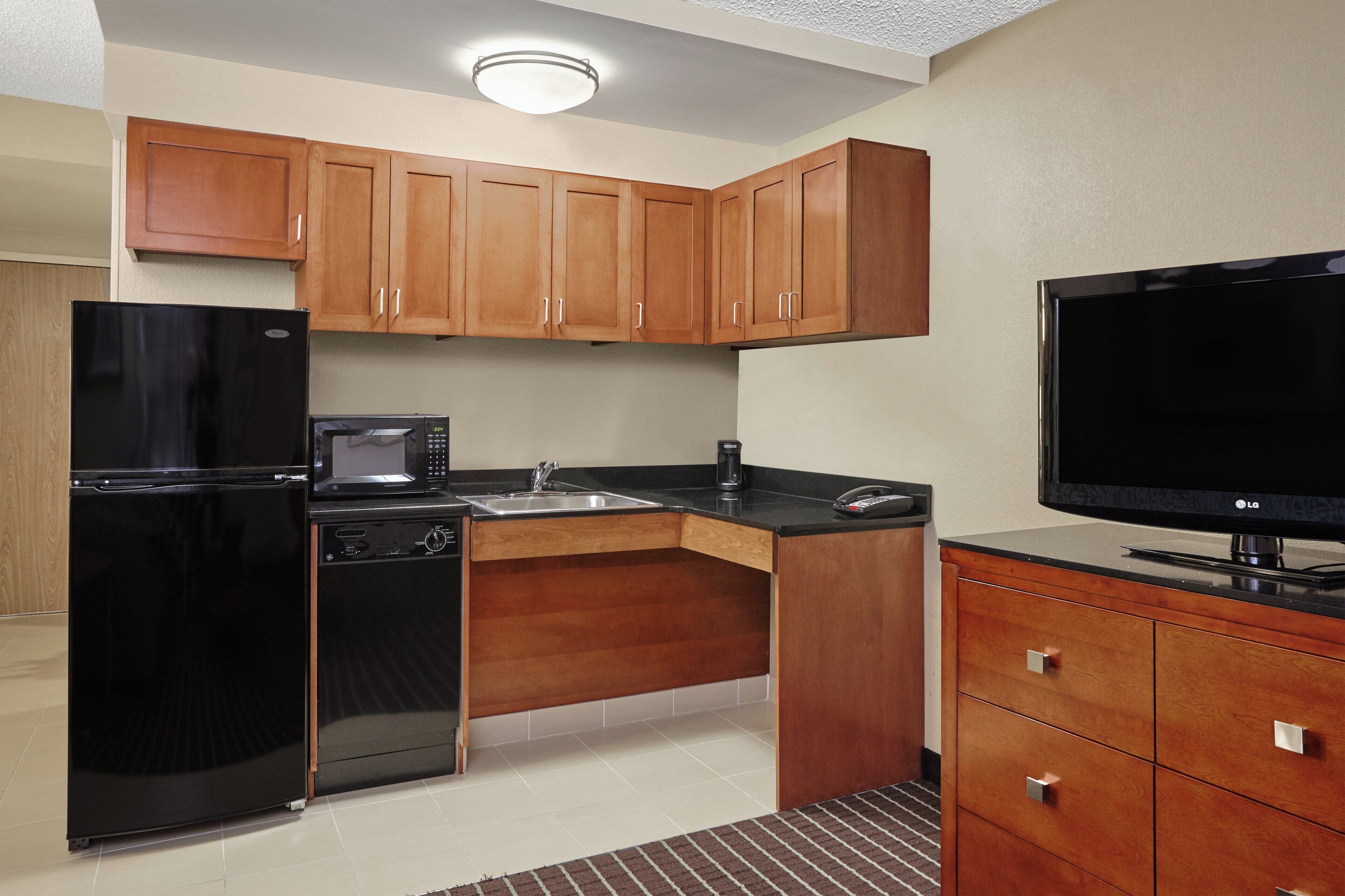 A compact kitchen with a refrigerator, microwave, coffee maker, and a flat-screen TV.
