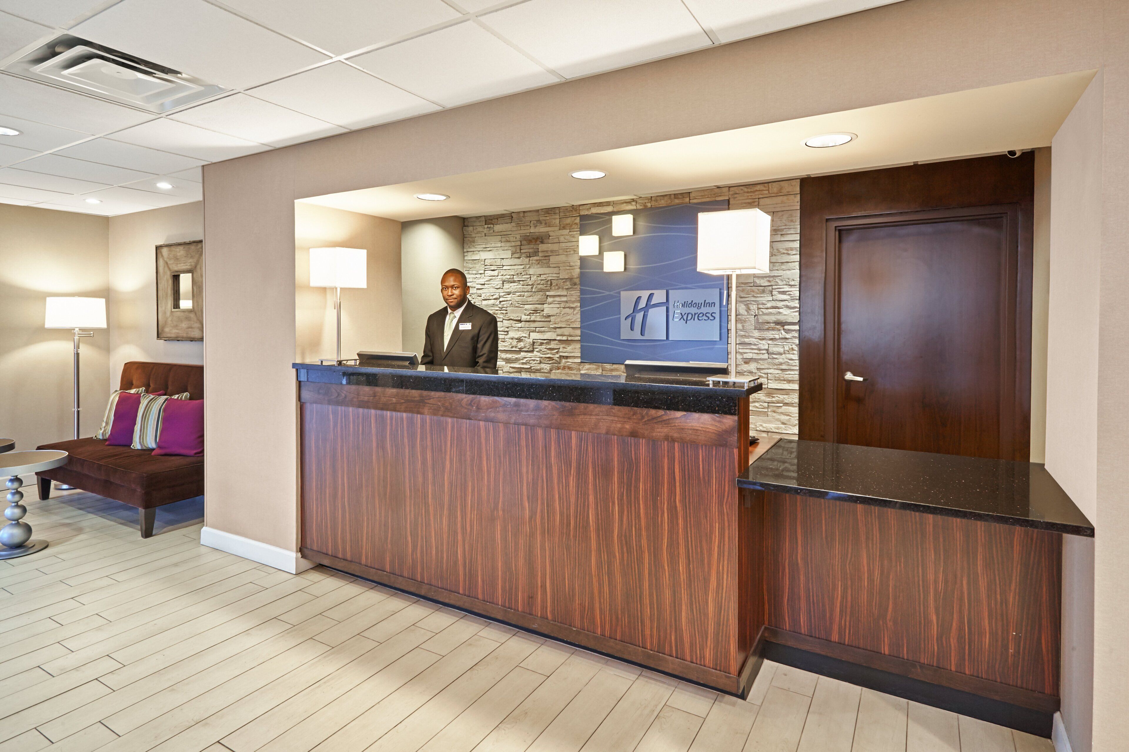 A hotel reception area with a wooden reception desk, a stone accent wall, and a closed door.