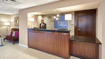 A hotel reception area with a wooden reception desk, a stone accent wall, and a closed door.
