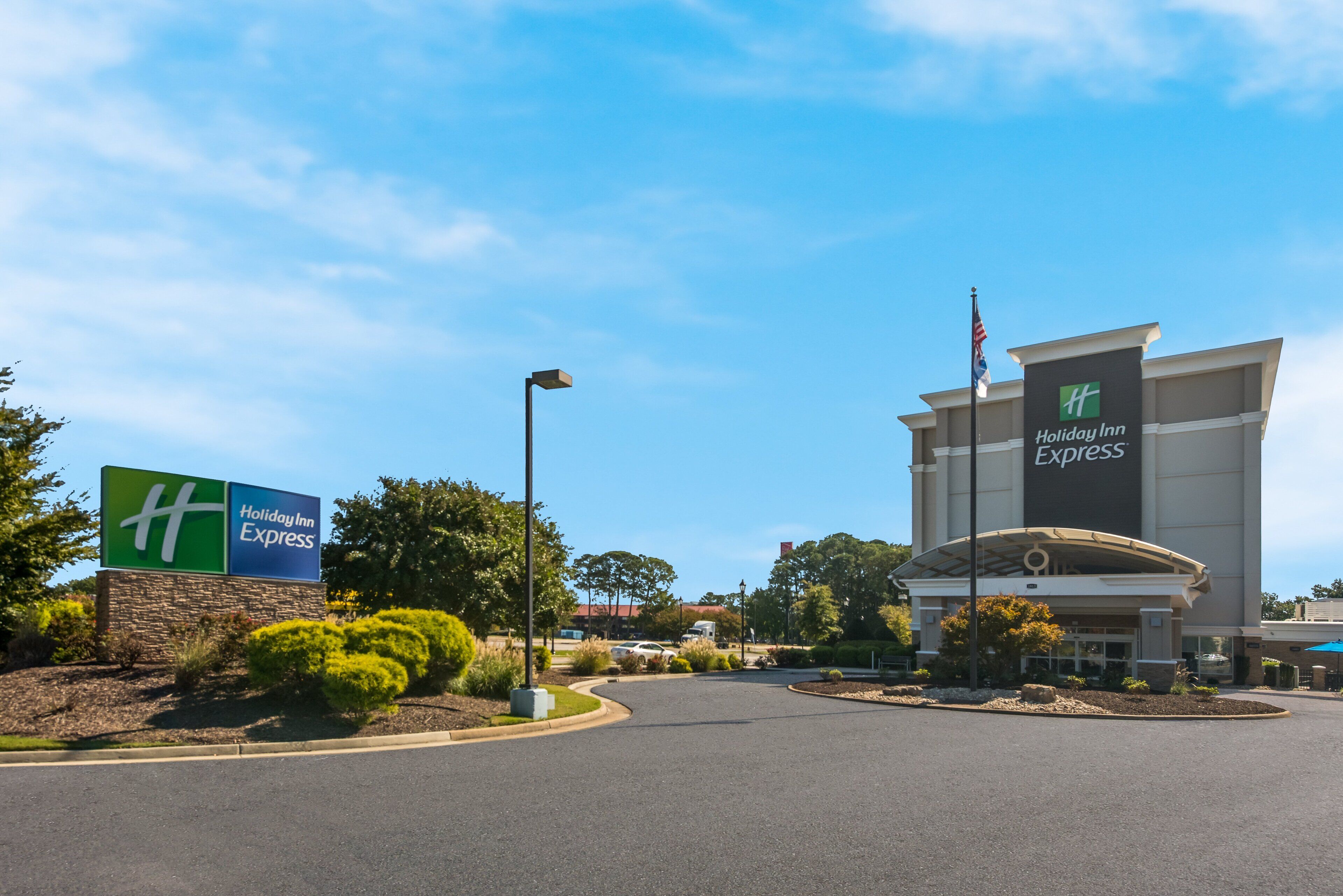 A Holiday Inn Express building with a clear sky, a landscaped entrance, and a parking area.