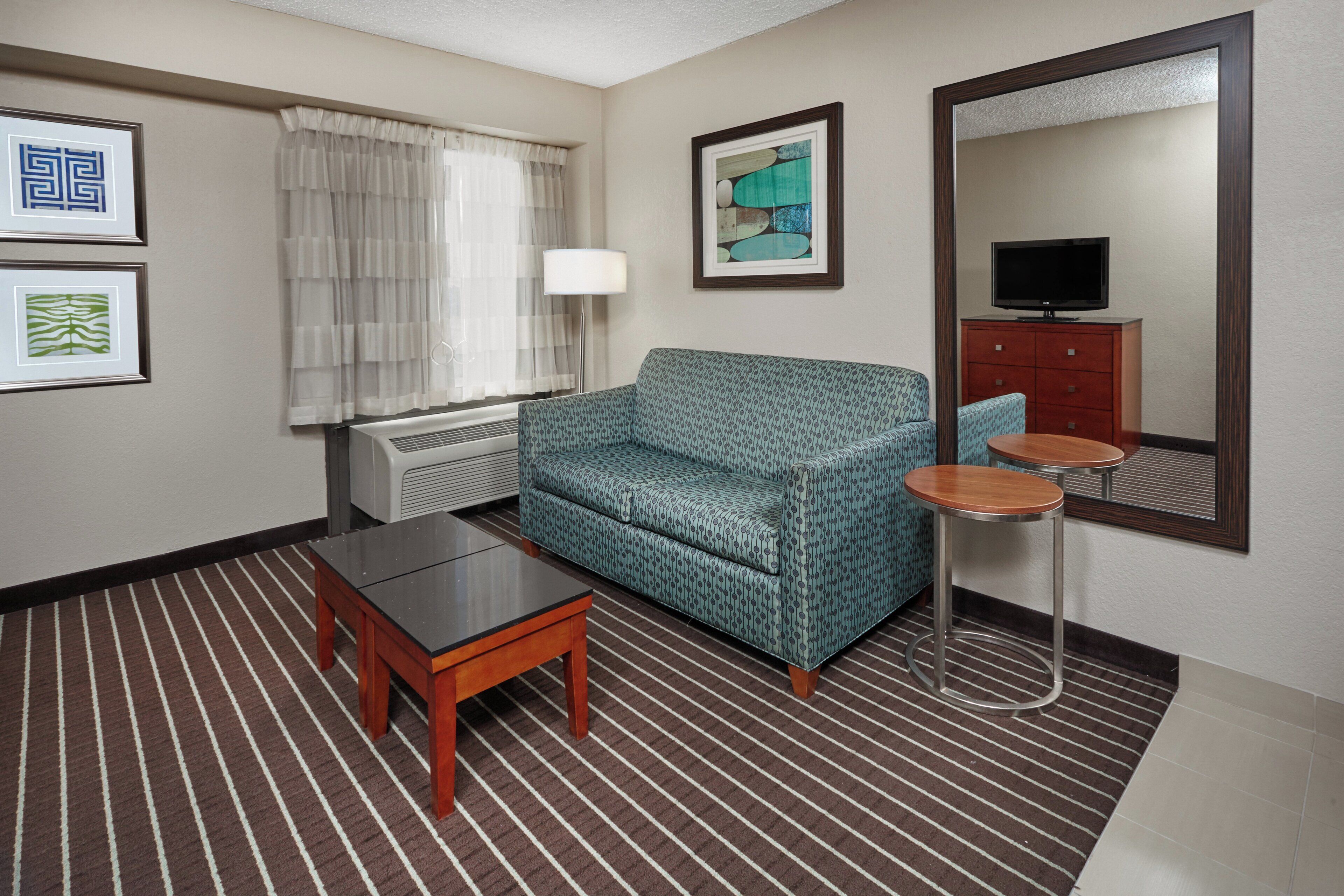 A hotel room with a sofa, a small table, a lamp, a television, and a mirror.