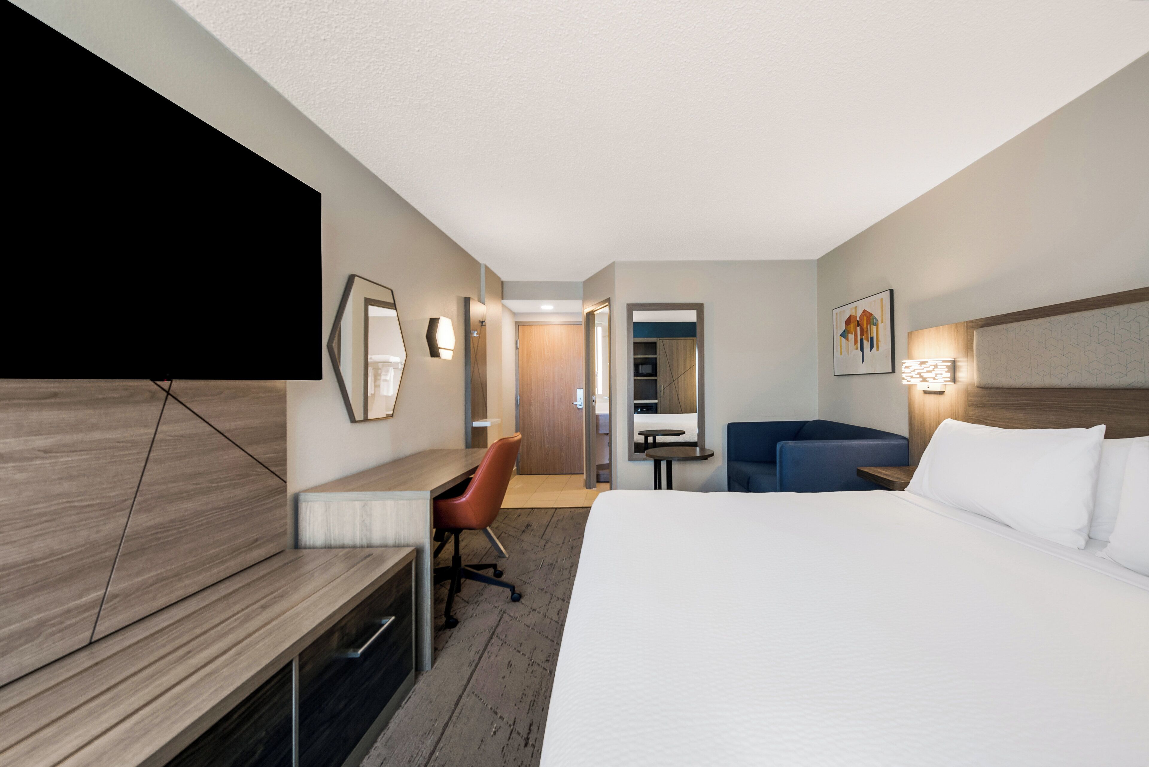 A hotel room with a bed, a desk, a chair, a sofa, and a TV.