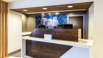 Un mostrador de recepción con diseño moderno, que presenta un panel frontal de madera y un motivo geométrico azul en la pared de fondo.