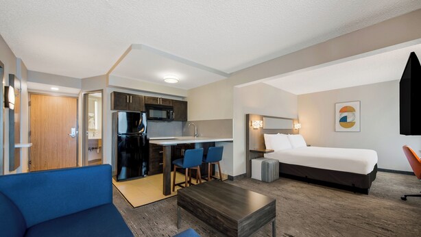 A compact hotel room with a kitchenette, a bed, a sofa, and a small table. - Holiday Inn Express Hampton - Coliseum Central by IHG (Hampton)