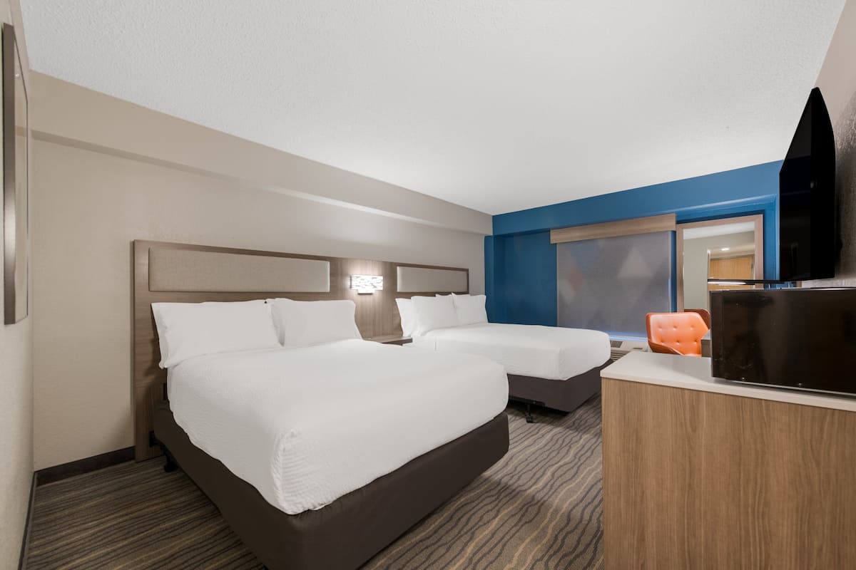 Two single beds with white linens and a wooden headboard, a flat-screen TV, and a desk with a chair.