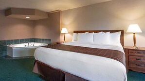 A hotel room with a large bed, a separate bathtub, two bedside lamps, and a wooden nightstand. - Ramada by Wyndham Bismarck (Bismarck)