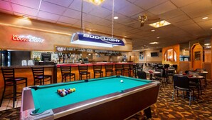 A pool table with a neon sign for Bud Light, a bar area with stools, and a seating area with tables and chairs. - Ramada by Wyndham Bismarck (Bismarck)