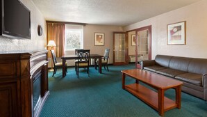 A hotel room with a TV, a sofa, a dining table with chairs, a fireplace, and artwork on the walls. - Ramada by Wyndham Bismarck (Bismarck)