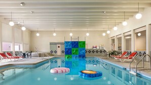 An indoor swimming pool with clear water, red lounge chairs, and a tiled wall with a colorful pattern. - Ramada by Wyndham Bismarck (Bismarck)