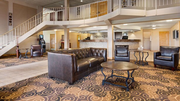 A spacious lobby with a central seating area, a staircase, and a kitchen in the background. - Ramada by Wyndham Bismarck (Bismarck)