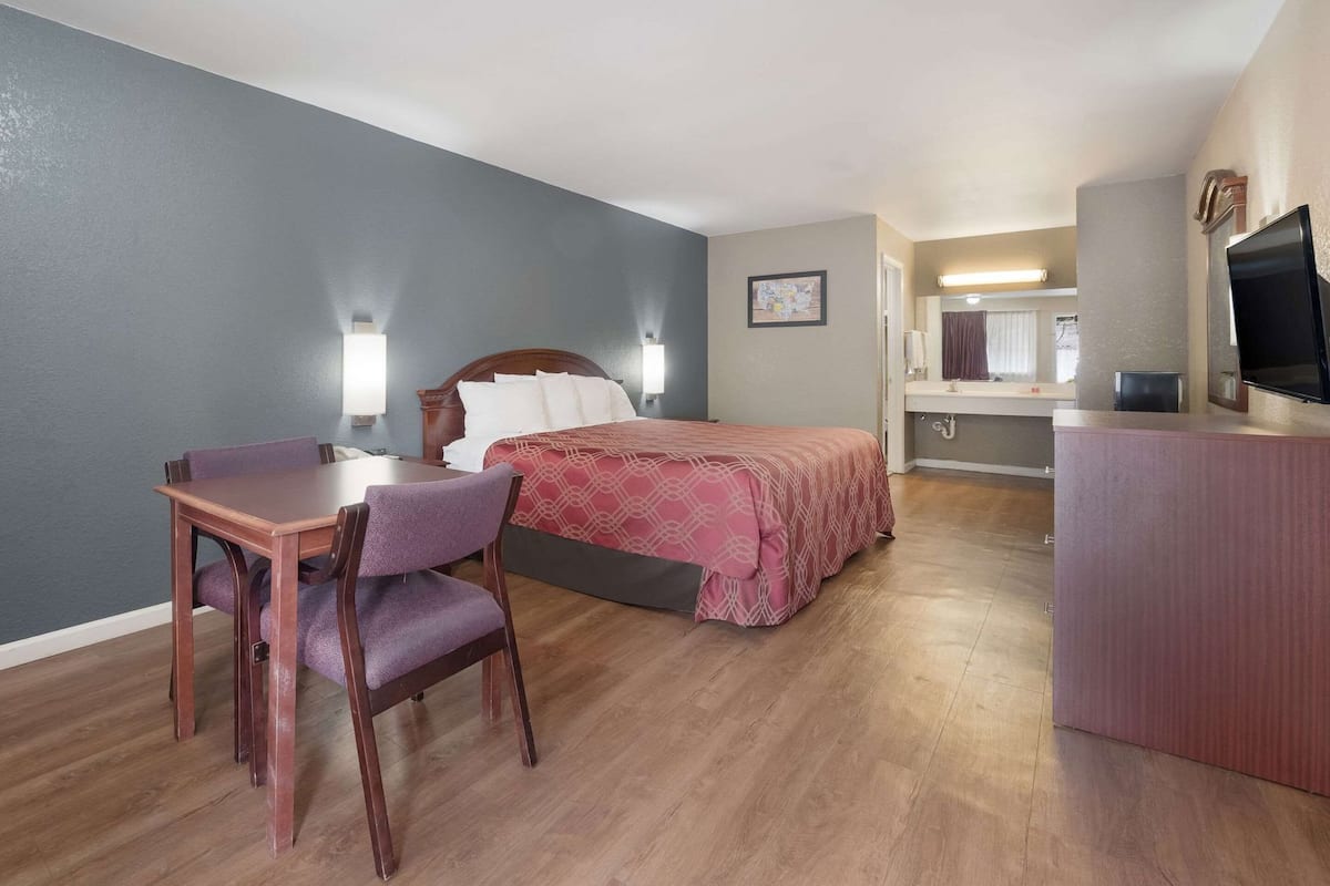 A hotel room with a bed, desk, chair, and a TV.