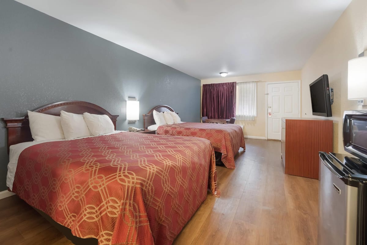 A hotel room with two beds, a TV, a desk, and a door.