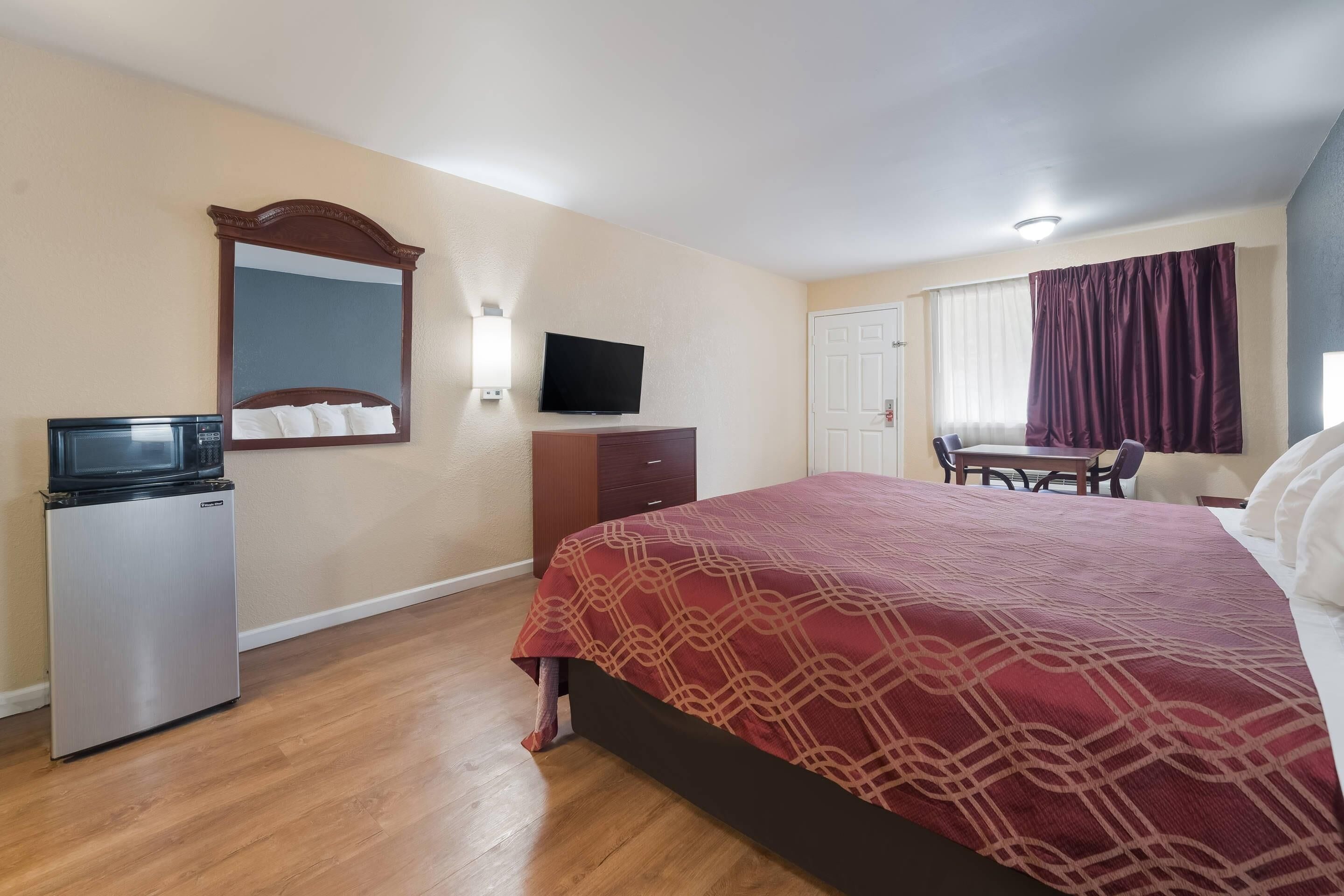 A hotel room with a bed, a television, a dresser, and a desk with a chair.
