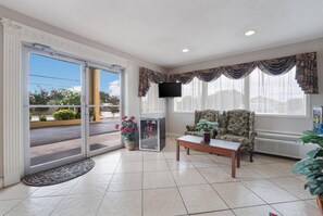 A hotel lobby with a sliding glass door, a television, a patterned armchair, a coffee table, and a potted plant. - Econo Lodge Thomaston (Thomaston)