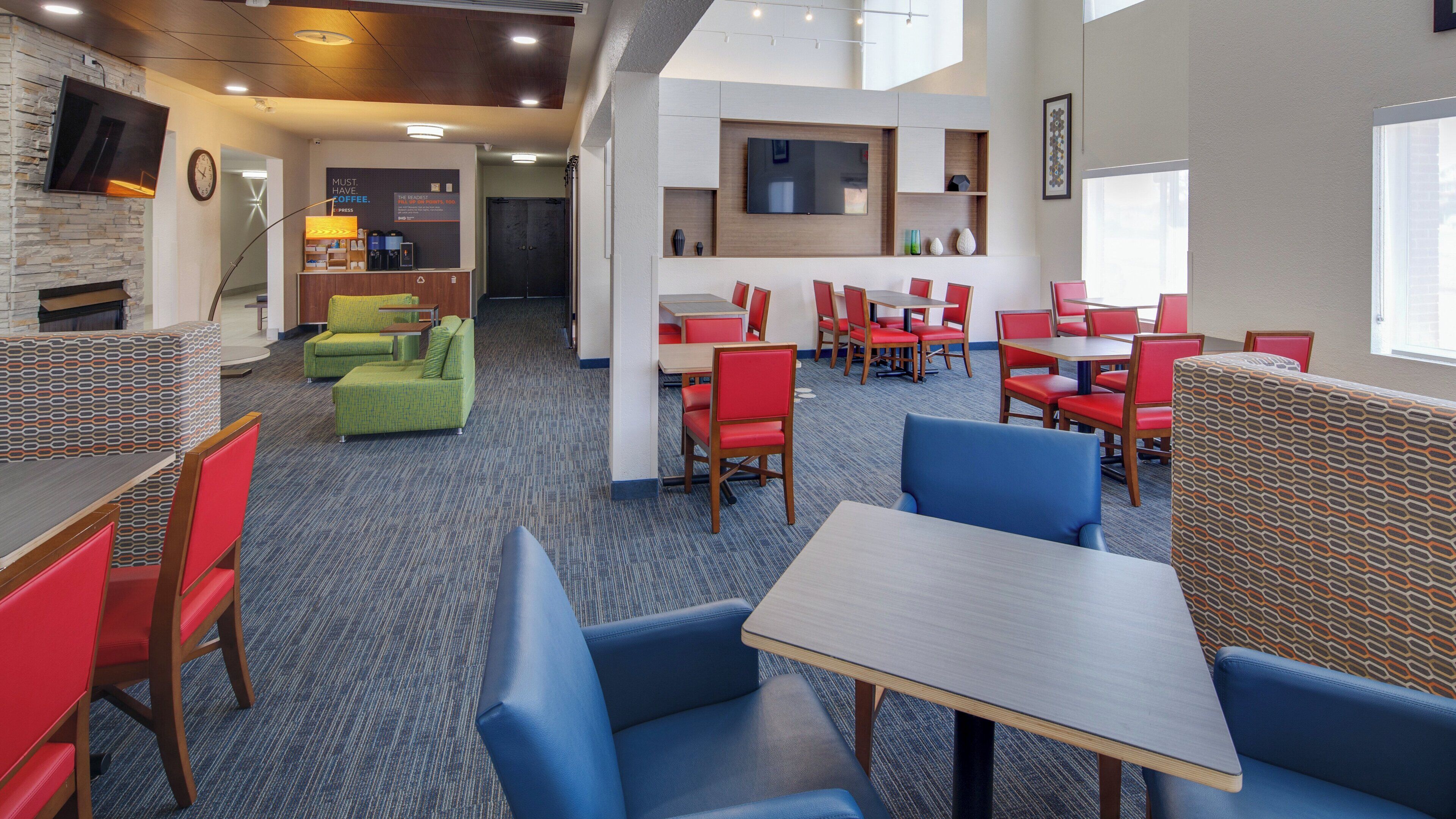 A modern hotel lobby with seating areas, a coffee station, and a TV mounted on the wall.