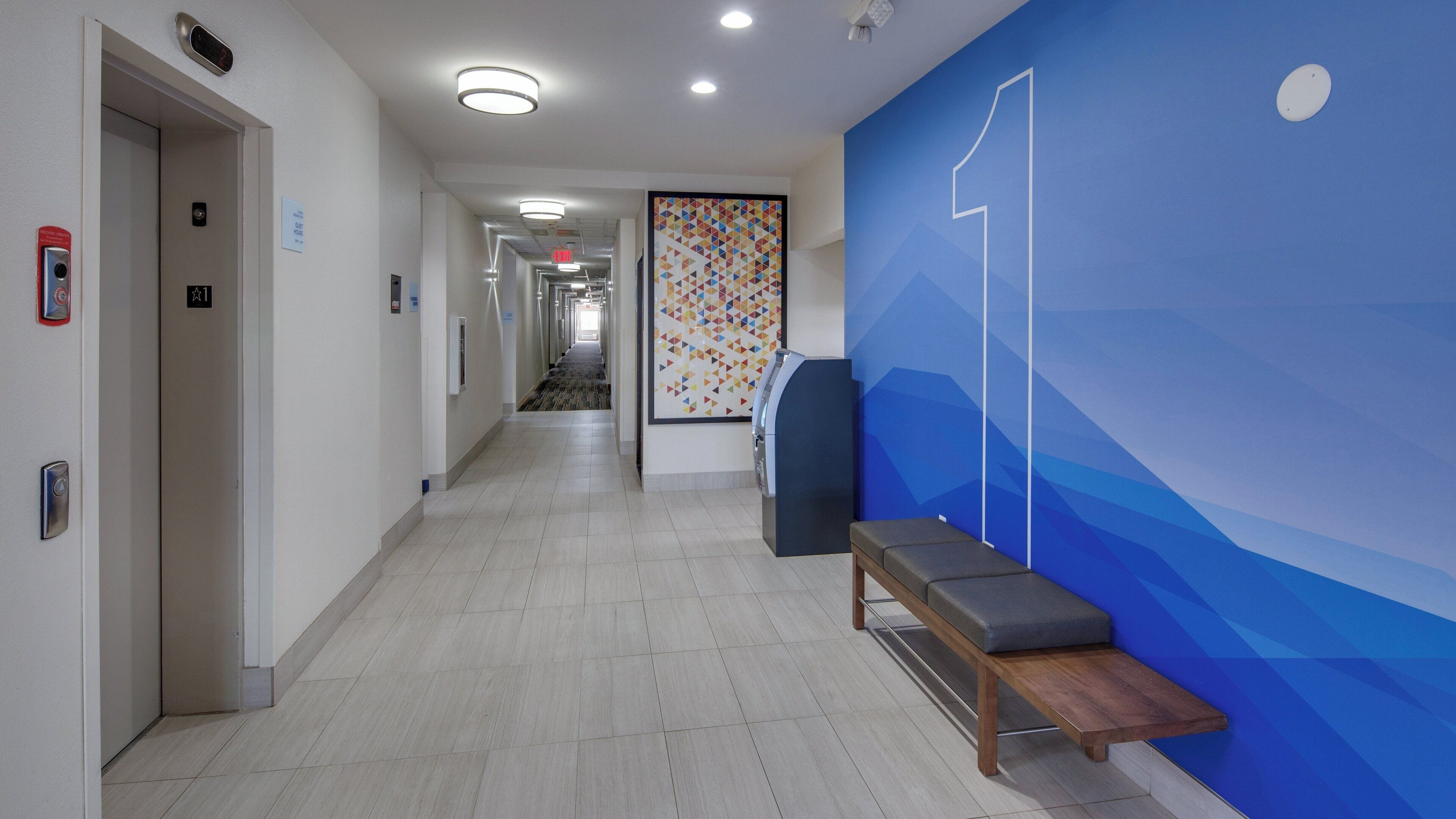 A hotel corridor with a bench, a wall with a geometric pattern, and an elevator.