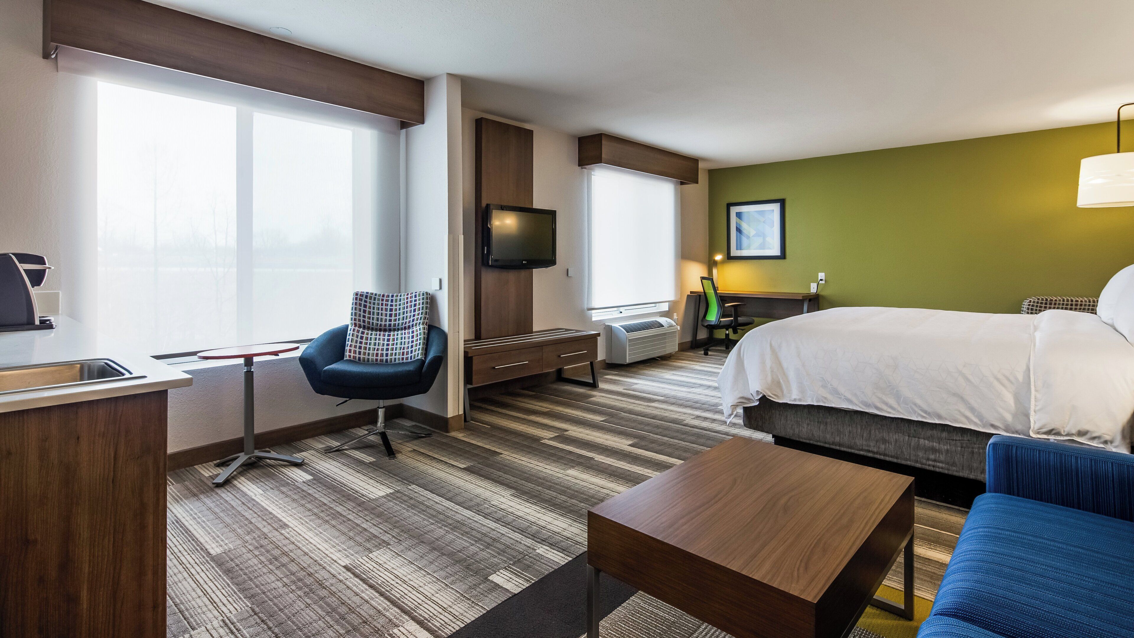 A hotel room with a bed, a desk, a chair, a TV, and a window.