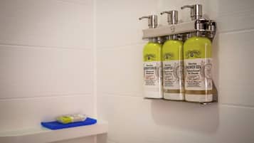 A bathroom with a white tiled wall, a shelf with three bottles of R. Watkins products, and a blue soap dish.