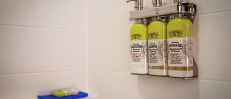 A bathroom with a white tiled wall, a shelf with three bottles of R. Watkins products, and a blue soap dish.