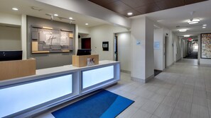 A hotel reception area with a reception desk, a digital screen, and a sign indicating 'The Market'. - Holiday Inn Express & Suites Detroit - Farmington Hills by IHG (Northville)