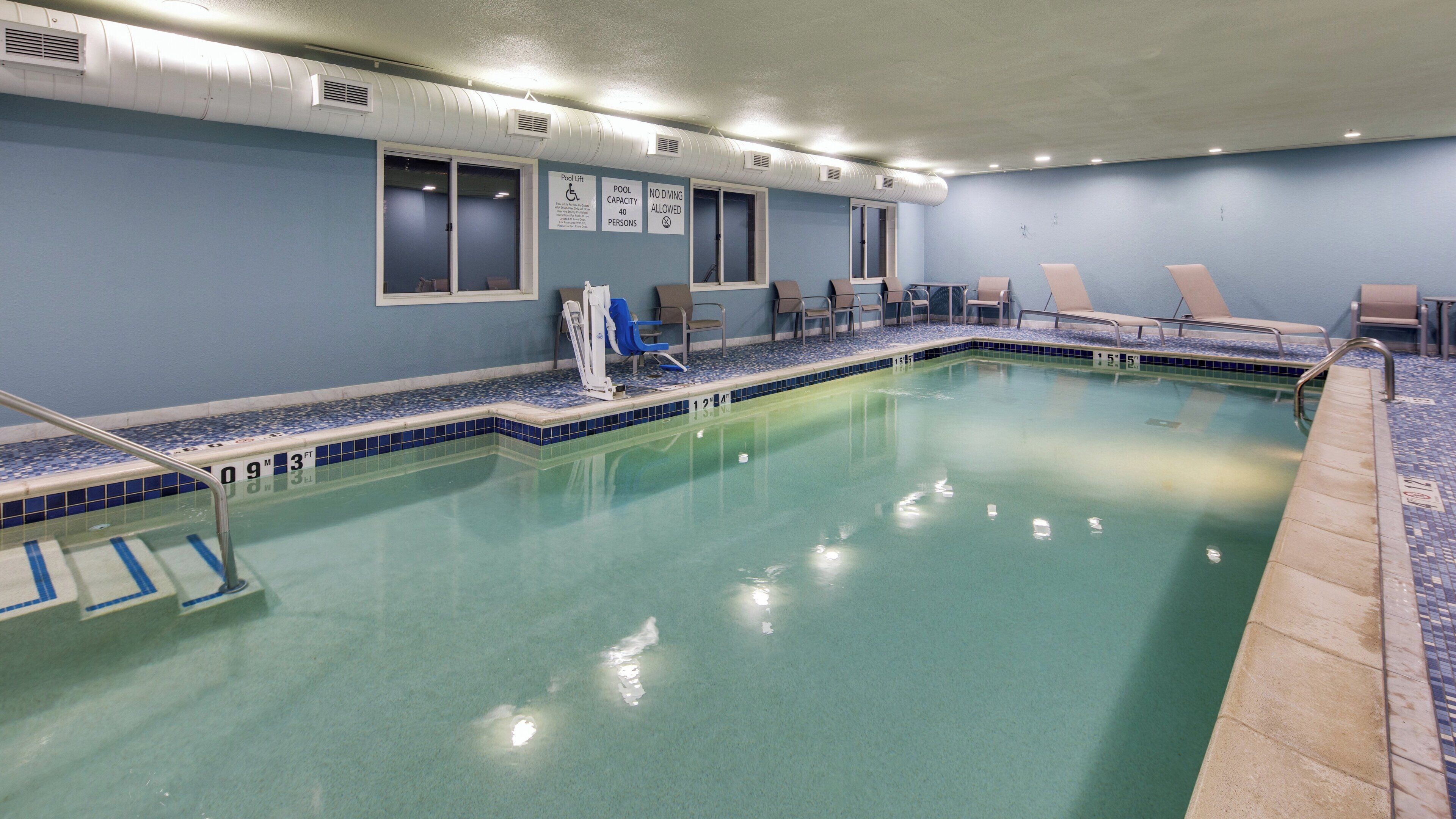 An indoor swimming pool with clear water, marked depth lines, and lounge chairs along the edge.
