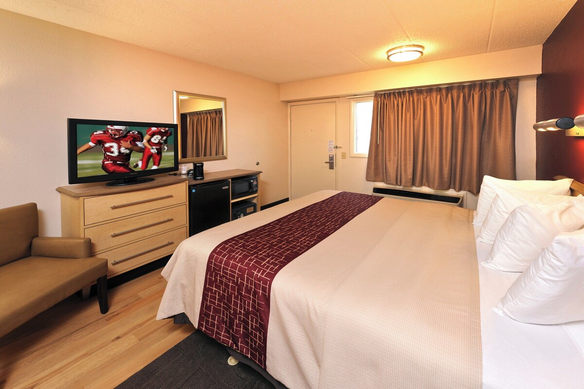 Une chambre d’hôtel avec un lit, une télévision, un bureau, une chaise et une fenêtre avec des rideaux.